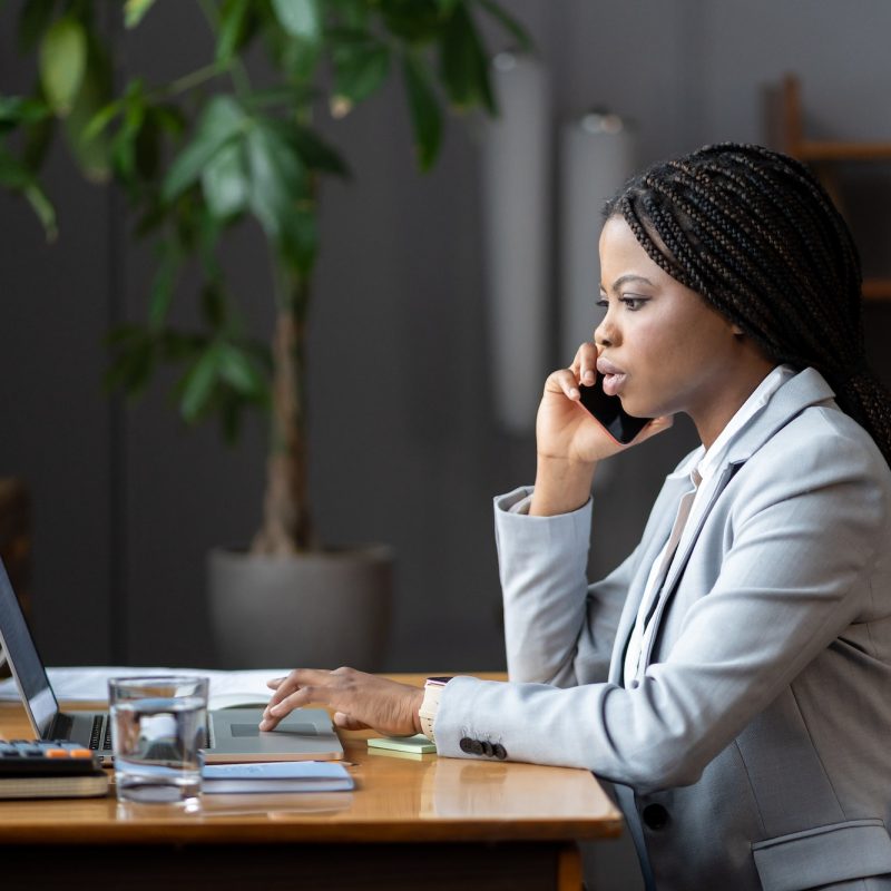 afro-female-business-consultant-interacting-with-client-over-phone-and-entering-data-on-laptop